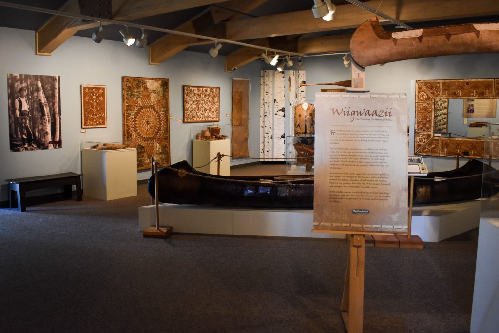 Another view of the center of the Wiigwaazii exhibit, revealing the historical canoe, wall art, and many baskets.