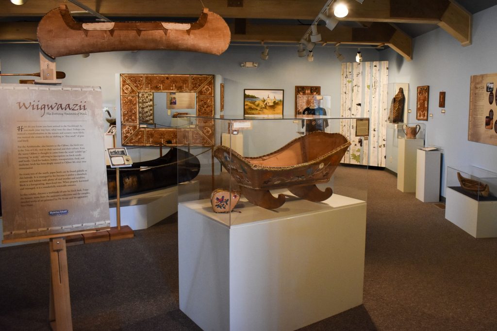 Many items from the exhibit are visible from this angle including the birchbark cradle, canoe, several wall pieces and some baskets.
