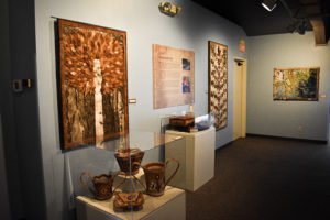 A view of the walls of Wiigwaazii Exhibit, featuring contemporary wall pieces and historic birchbark baskets