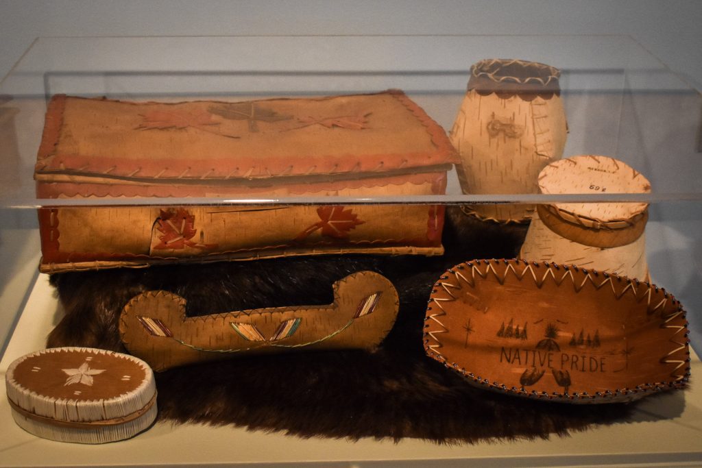 A variety of birchbark items, and box decorated with maple leaves. A small canoe also decorated and several baskets of various sizes.