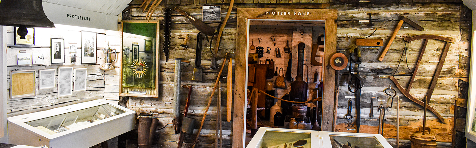 Rough wood walls, some painted white, some their original color are lined with artefacts from early settler history in Madeline Island. Pioneer Home and part of the Religious exhibit at Madeline Island Museum