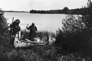 A historical photograph of Ojibwe launching a birchbark canoe