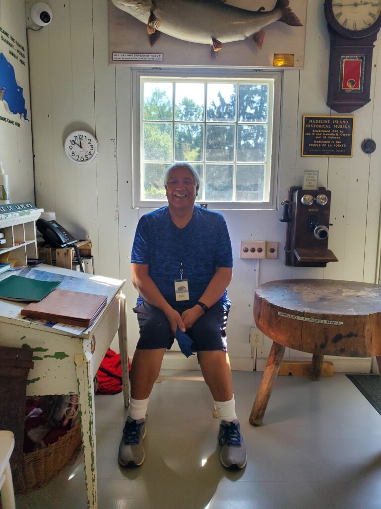 Rob the interpreter sitting on a stool while giving guests a Indigenous perspective on Madeline Island history during his employment.